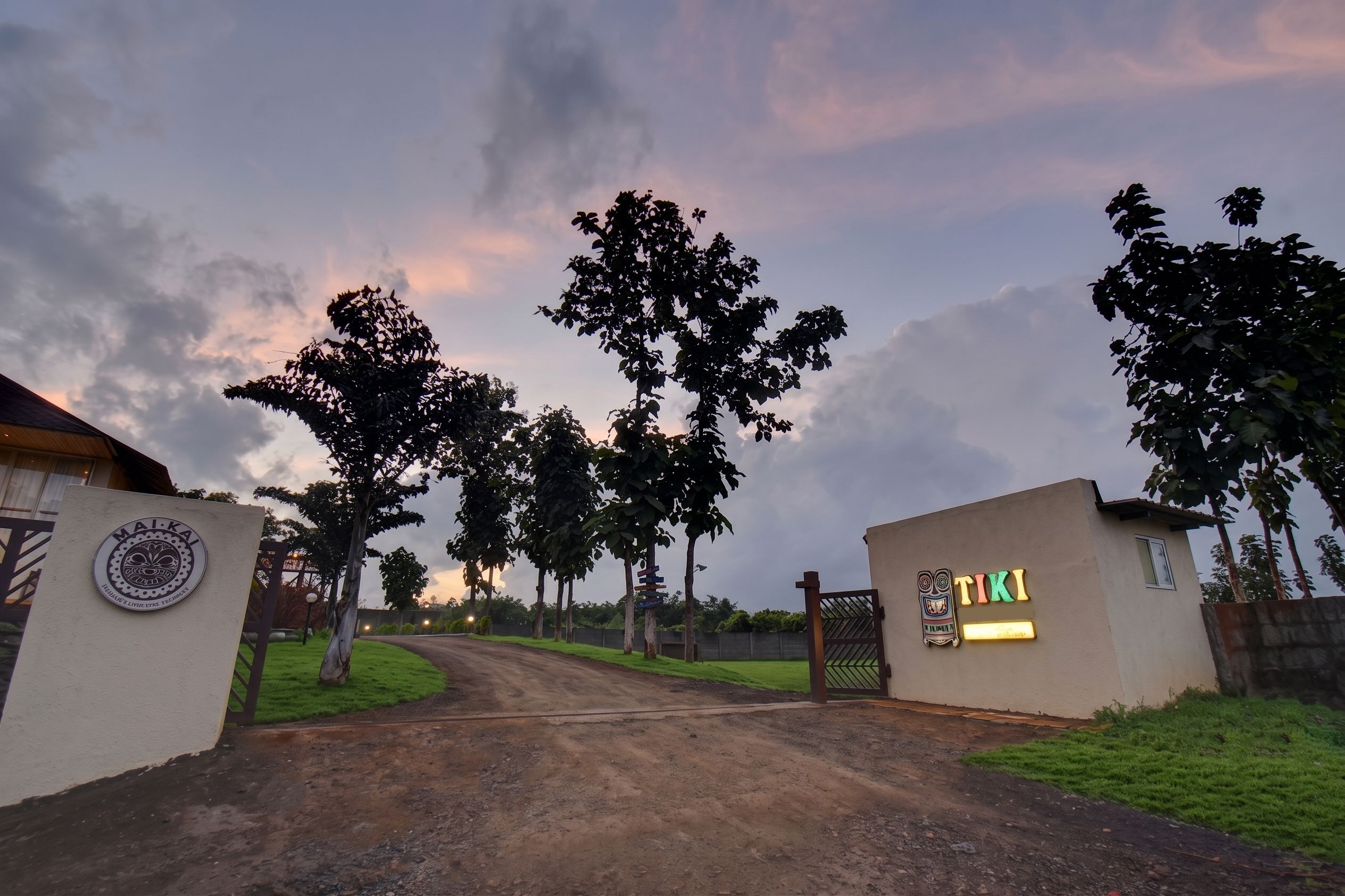 A gated entrance with a signboard, a pathway leading to a building, and trees lining the path.