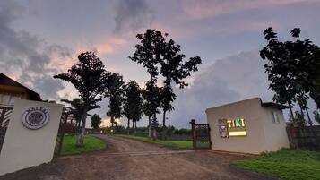 A gated entrance with a signboard, a pathway leading to a building, and trees lining the path.