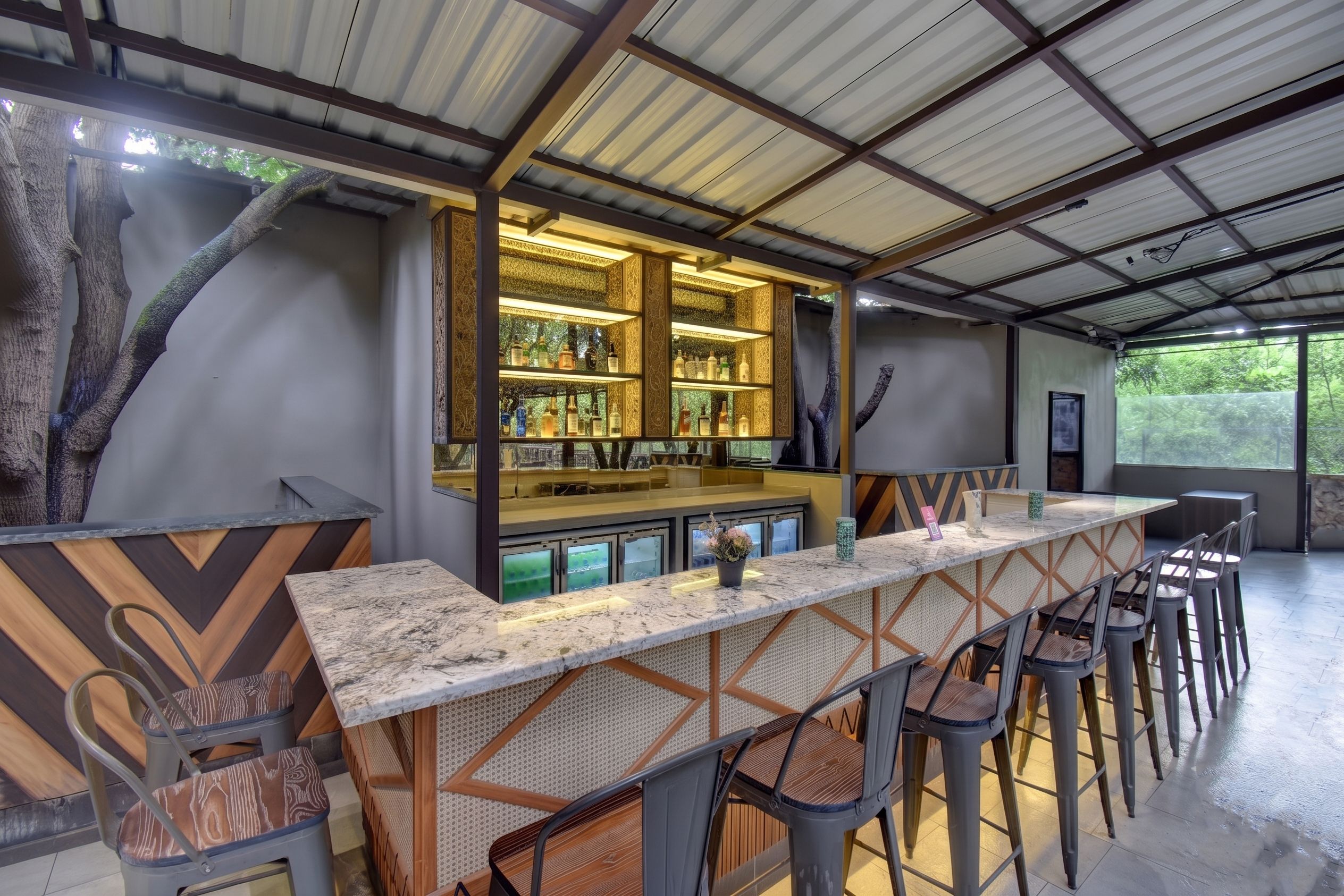 Zona de bar con una barra larga, varios taburetes y una exhibición de botellas.