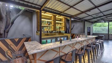 Zona de bar con una barra larga, varios taburetes y una exhibición de botellas.