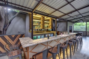 Zona de bar con una barra larga, varios taburetes y una exhibición de botellas.