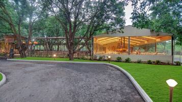A restaurant with a glass enclosure, surrounded by trees and a gravel path.