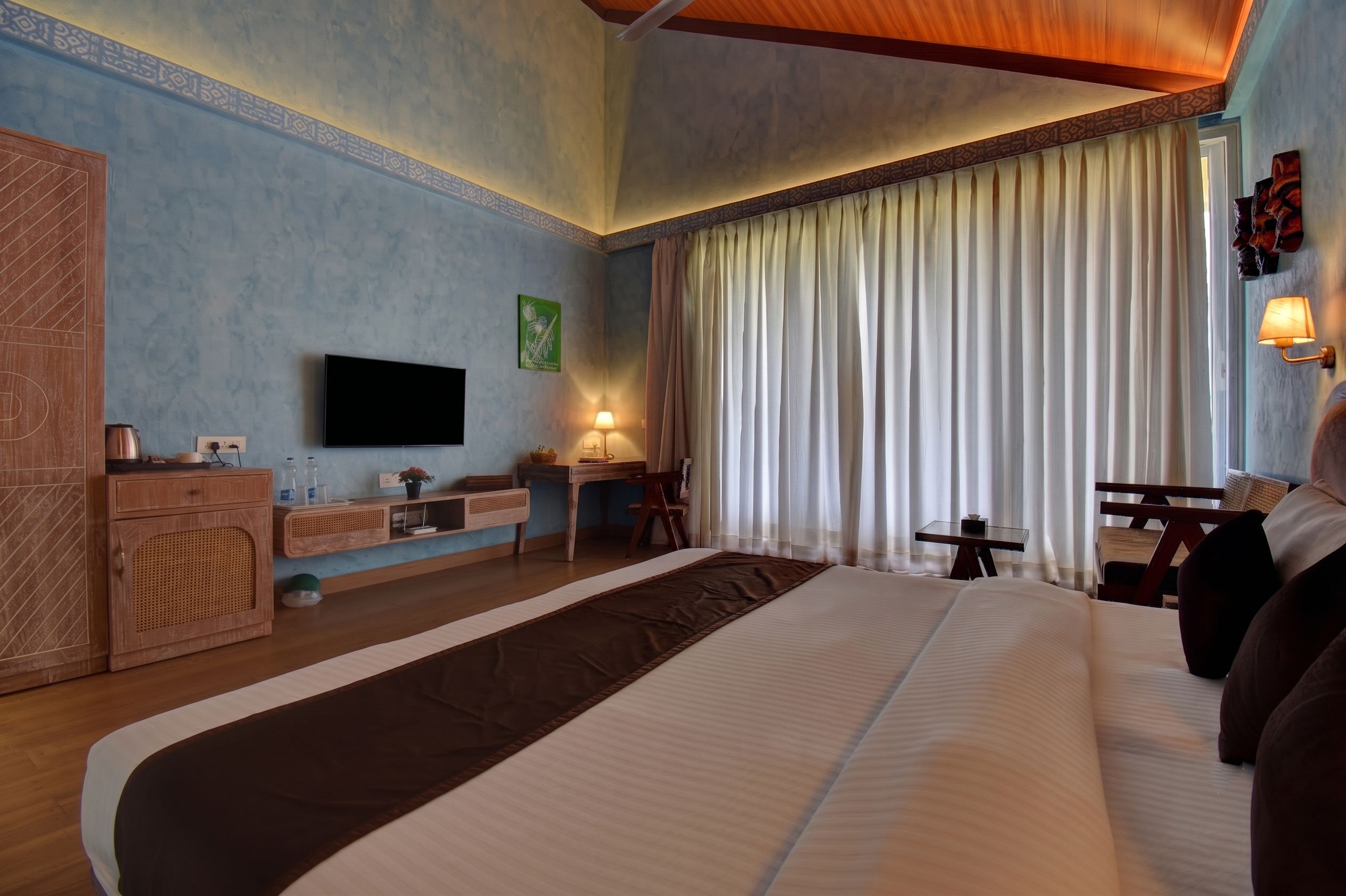 A hotel room with a large bed, a desk, a television, and a window with curtains.