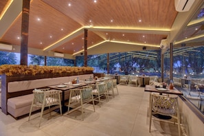 An indoor dining area with wooden ceiling, cushioned seating, and tables set for dining.