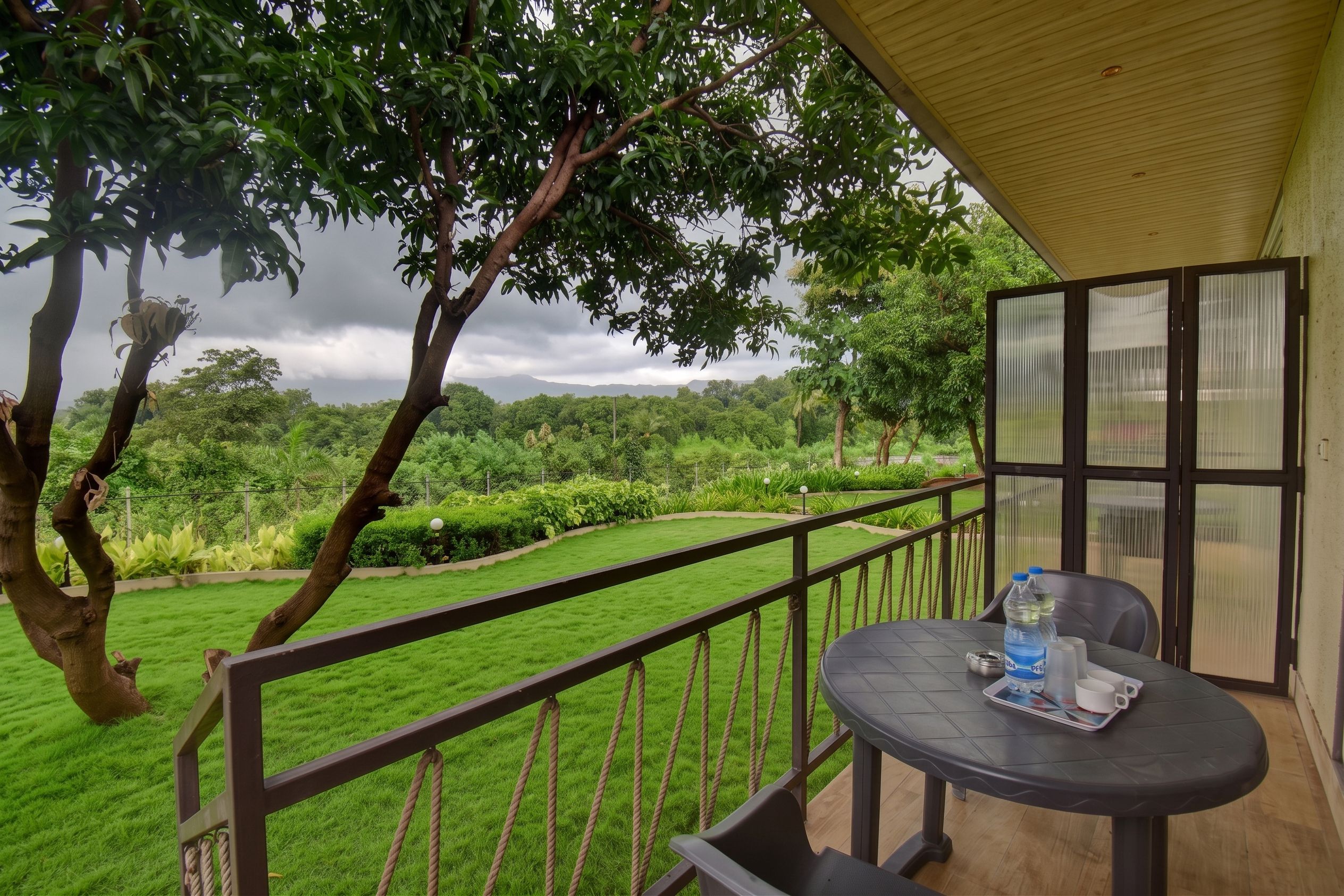 A balcony with a table and chairs, overlooking a lush green landscape with trees and a distant view of mountains.