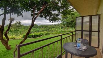 A balcony with a table and chairs, overlooking a lush green landscape with trees and a distant view of mountains.