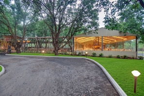 A modern building with large glass windows, surrounded by lush greenery and trees.