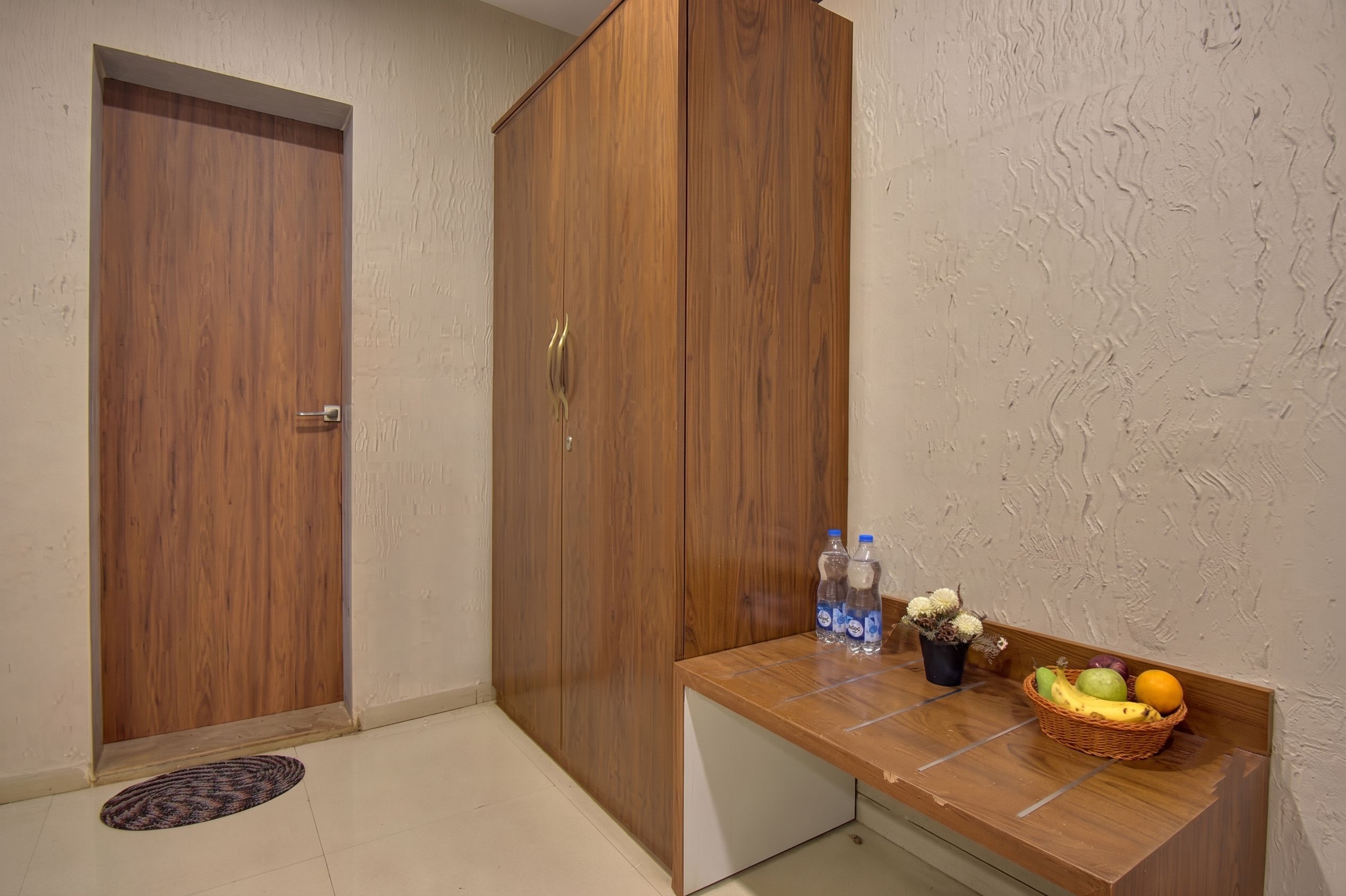 A room with a wooden wardrobe, a small table with water bottles and a fruit basket.