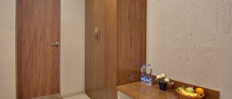 A room with a wooden wardrobe, a small table with water bottles and a fruit basket.