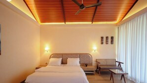 A bedroom with a bed, a chair, a nightstand, and a ceiling fan. - Tiki Farms – Polynesian Boutique Resort, Karjat (Karjat)