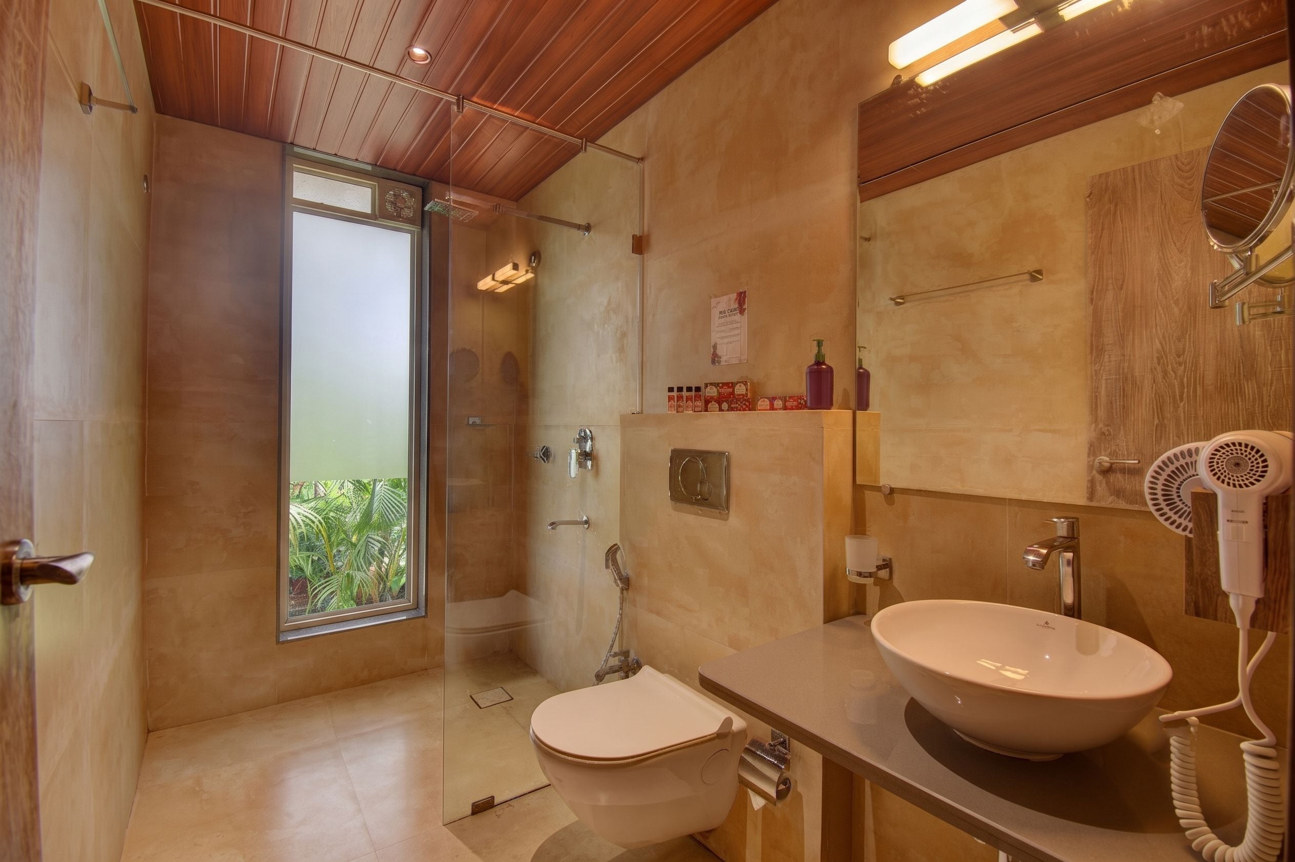 Un baño moderno con un ventanal grande, ducha, inodoro, lavamanos con espejo y secador de pelo.
