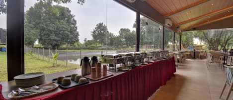 A buffet setup with a long table covered in a red tablecloth, serving dishes, and utensils.
