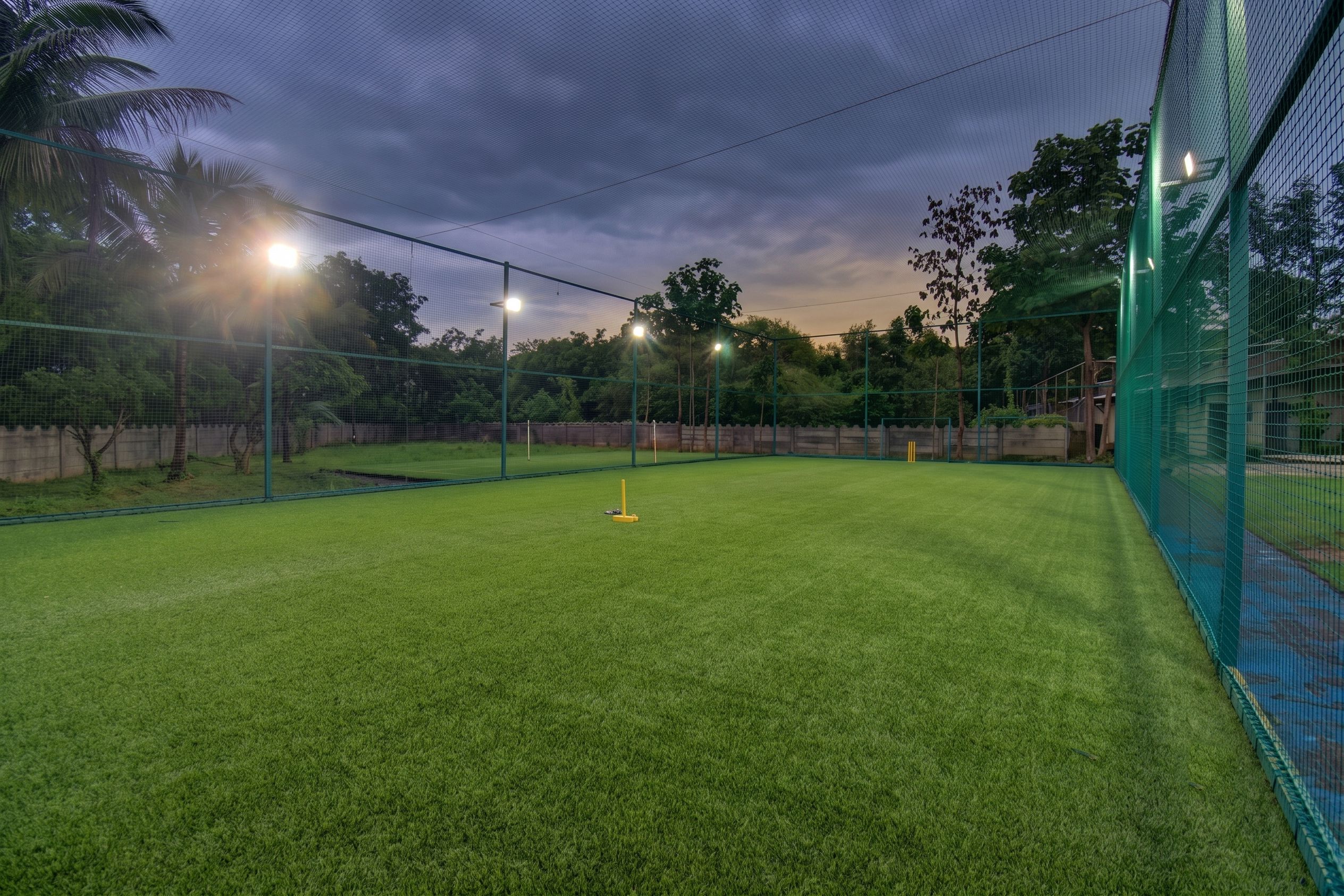 Un campo de críquet al aire libre con una valla de protección y luces artificiales.