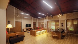 A spacious living area with a wooden reception desk, seating arrangements, and a TV. - Tiki Farms – Polynesian Boutique Resort, Karjat (Karjat)