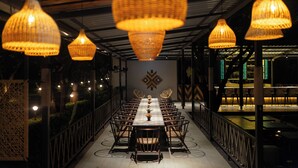 A long dining table with chairs, overhead wicker lamps, and a decorative wall pattern. - Tiki Farms – Polynesian Boutique Resort, Karjat (Karjat)
