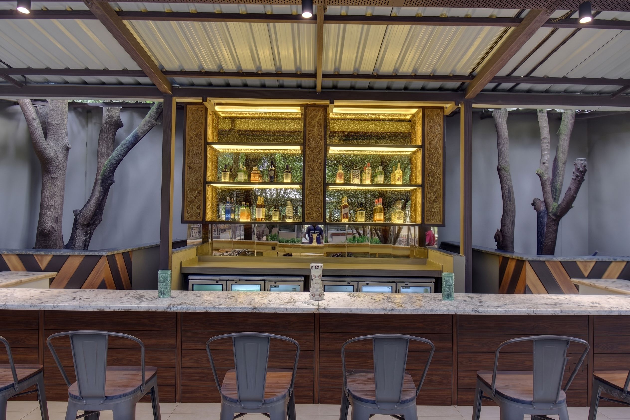 A bar area with a counter, shelves of bottles, and chairs.