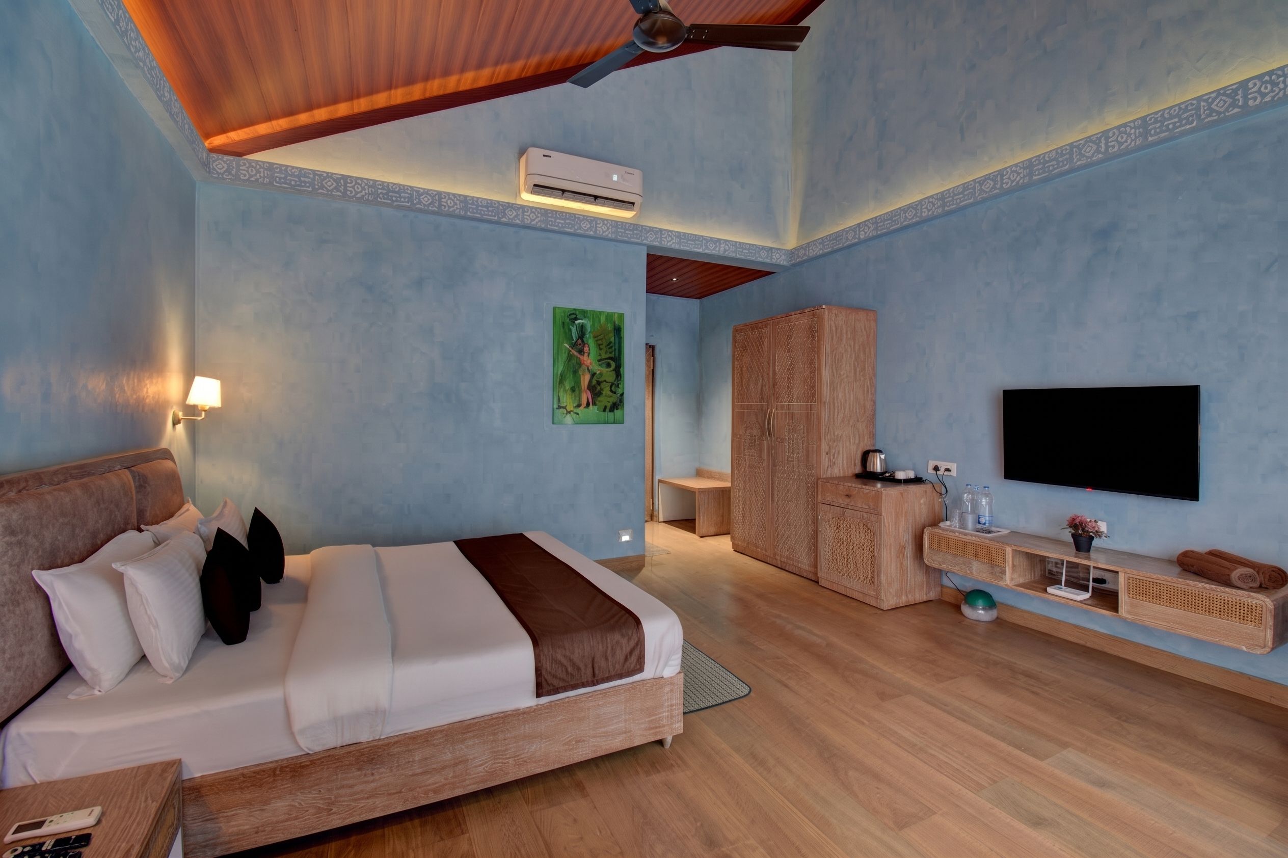 A hotel room with a bed, a desk, a wardrobe, a television, and an air conditioning unit.