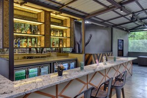 Zona de bar con una barra larga, múltiples estantes llenos de botellas y un diseño moderno con patrones geométricos en las paredes.