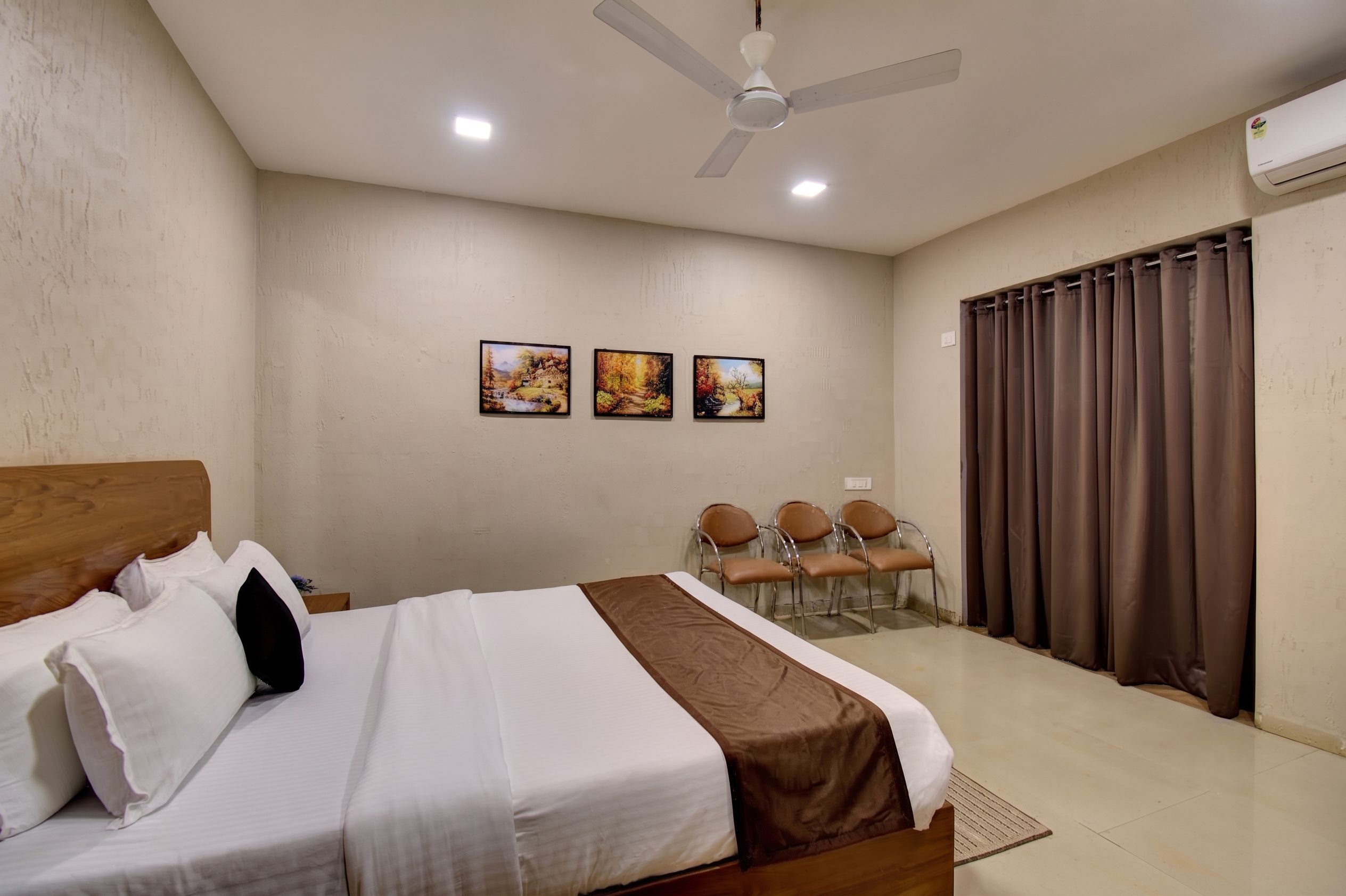 Habitación de hotel con cama, ventilador de techo, zona de estar con sillas y tres cuadros colgados en la pared.