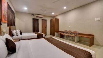 A hotel room with two beds, a desk, chairs, a ceiling fan, and an air conditioning unit.