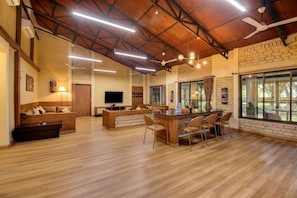 A spacious living area with a wooden ceiling, a dining table with chairs, a sofa, and a television.