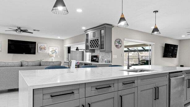 A modern kitchen with grey cabinets, a large island, and pendant lighting. - Relaxing Retreat, Heated Pool,  Gulf Access NEW (Cape Coral)