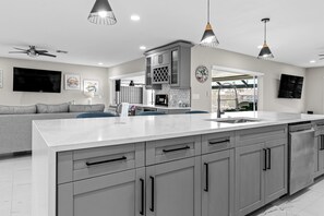 A modern kitchen with grey cabinets, a large island, and pendant lighting. - Relaxing Retreat, Heated Pool,  Gulf Access NEW (Cape Coral)