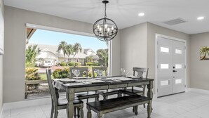 A dining area with a table set for four, a bench, and a chandelier. - Relaxing Retreat, Heated Pool,  Gulf Access NEW (Cape Coral)