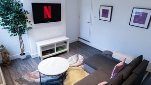 Ein modernes Wohnzimmer mit flachbildfernseher an der Wand, einer weißen Unterhaltungsecke, einem grauen Sofa, einem runden Couchtisch und einem gemusterten Teppich.