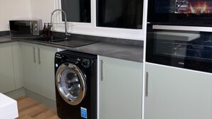 A compact kitchen with a washing machine, a microwave, and an oven. - House-sleeps8-parking-garden (Leeds)