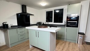 A modern kitchen with a central island, built-in oven, and a window. - House-sleeps8-parking-garden (Leeds)