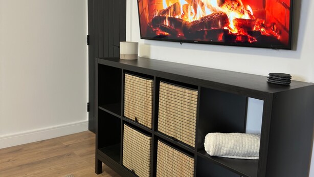 A modern living room with a flat-screen TV mounted on the wall displaying a fireplace image. - House-sleeps8-parking-garden (Leeds)