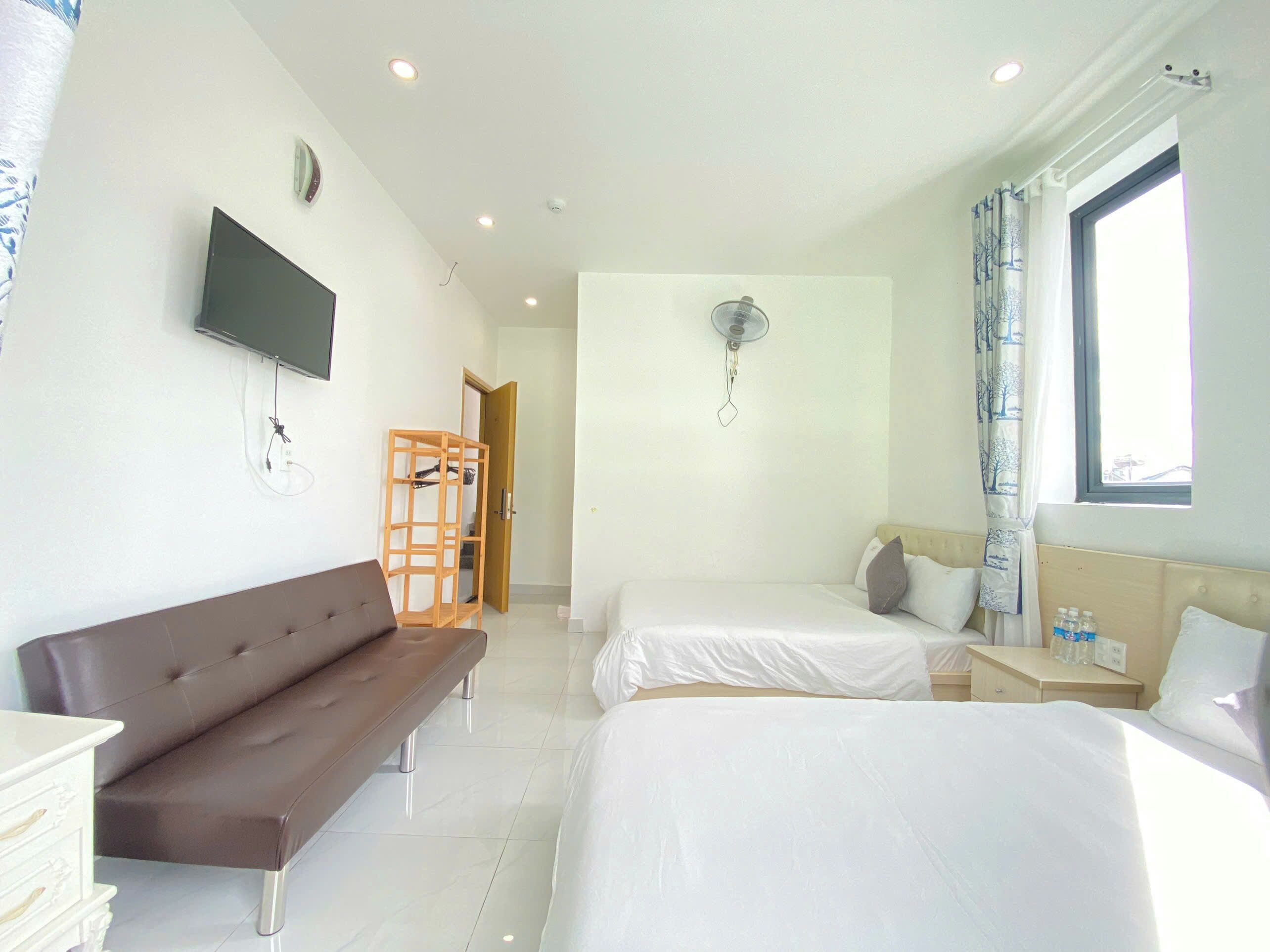 A hotel room with a sofa, two beds, a TV, a ceiling fan, and a window with curtains.