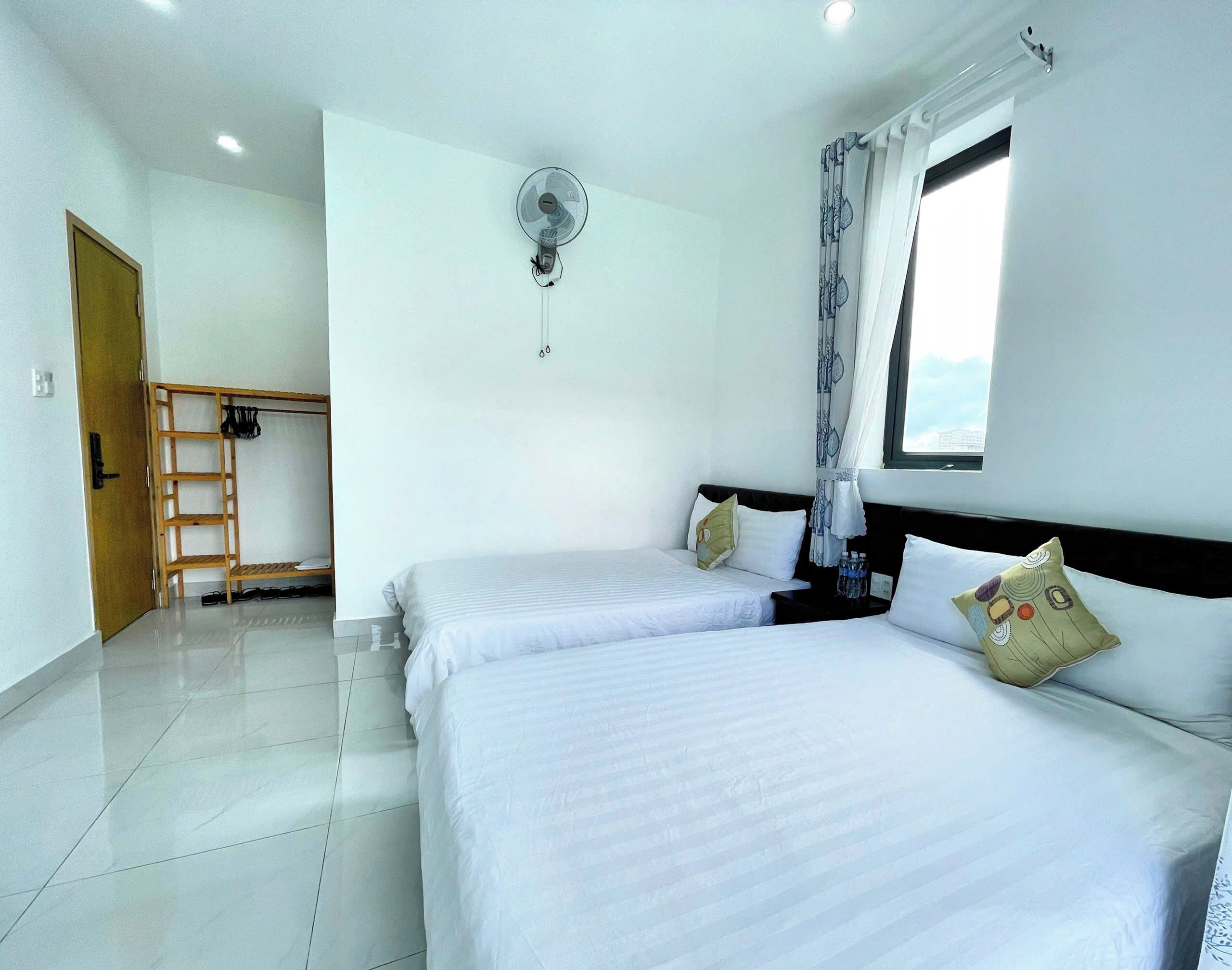 A hotel room with two beds, a wooden ladder, a ceiling fan, and a window with curtains.