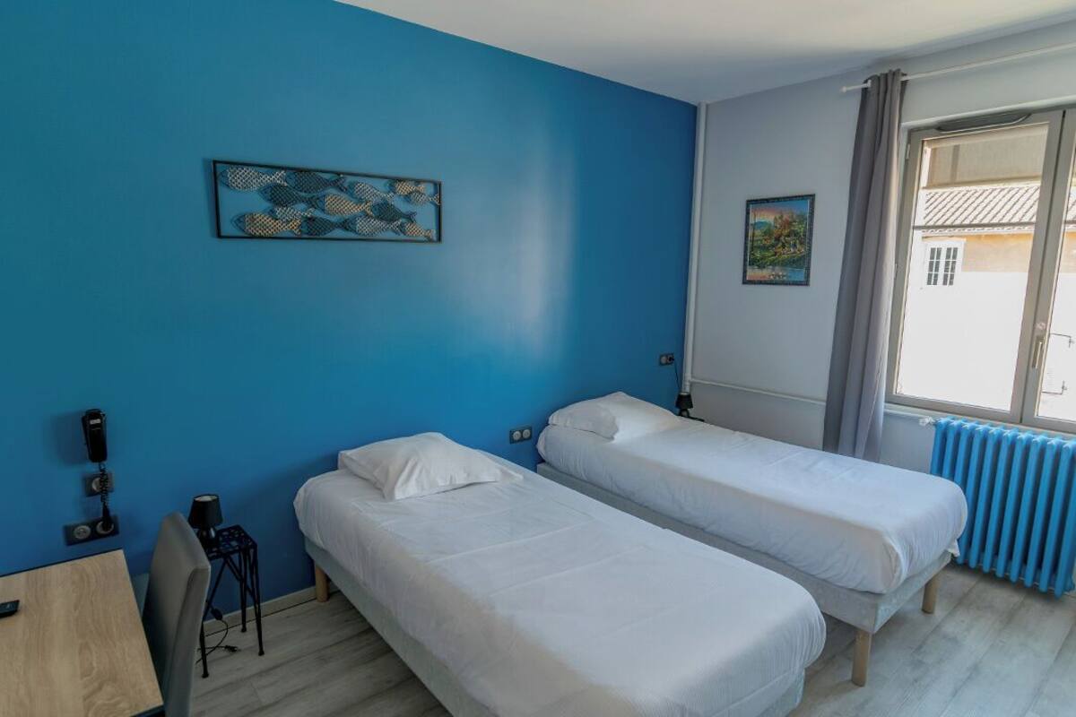 Een kamer met twee eenpersoonsbedden, een bureau met stoel, een tafeltje en een radiator.