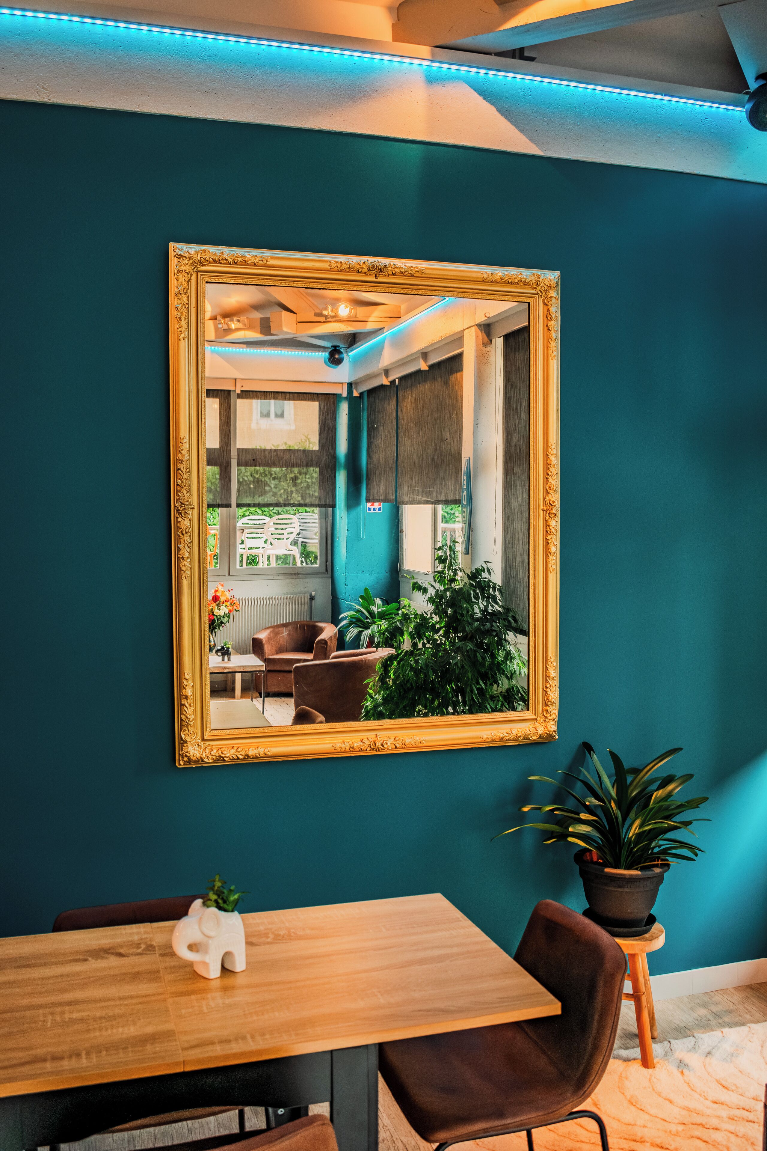 A teal-walled room with a wooden dining table, a brown chair, a small elephant-shaped plant, and a potted plant.