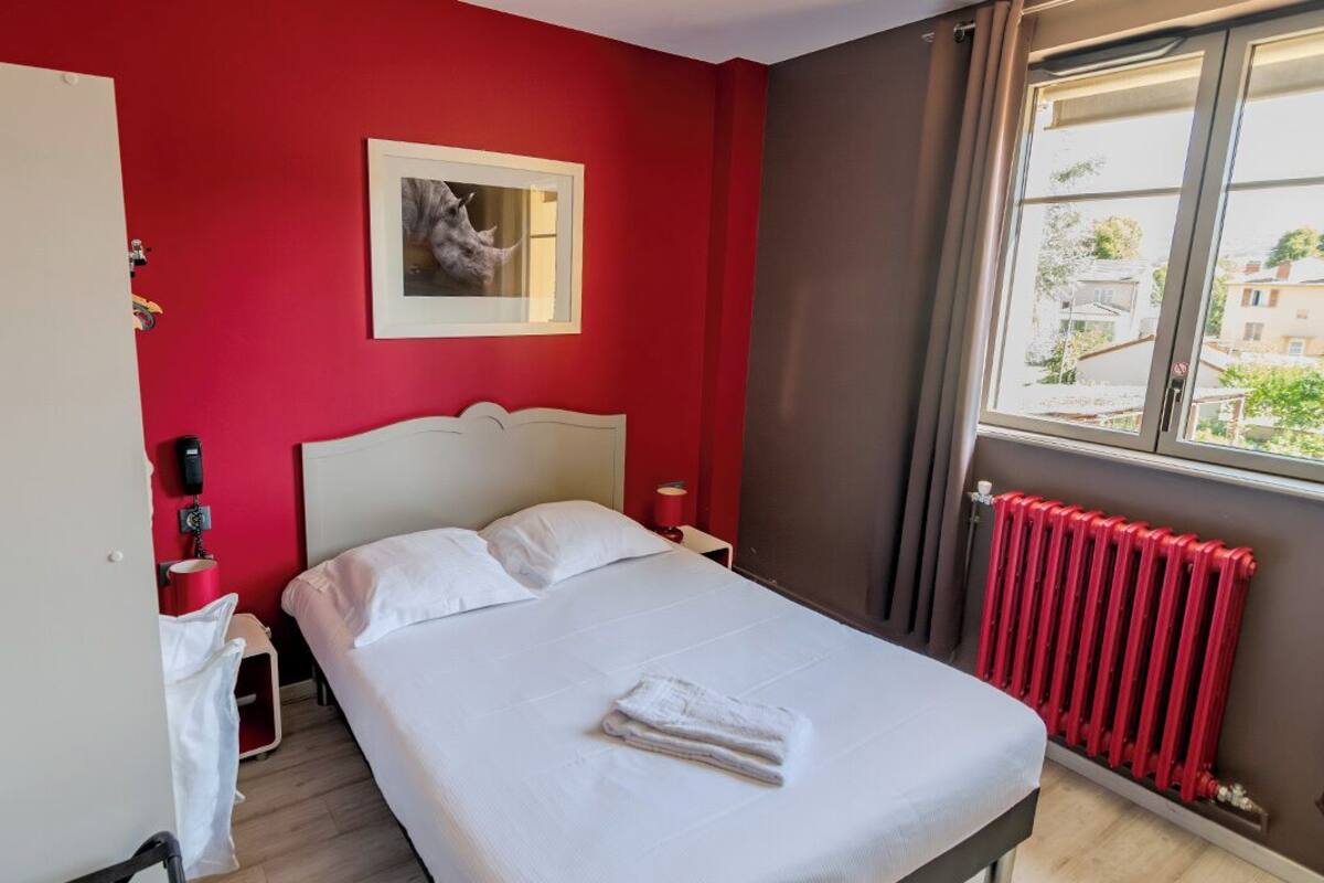 Een hotelkamer met een bed, een rode muur, een raam en een radiator.