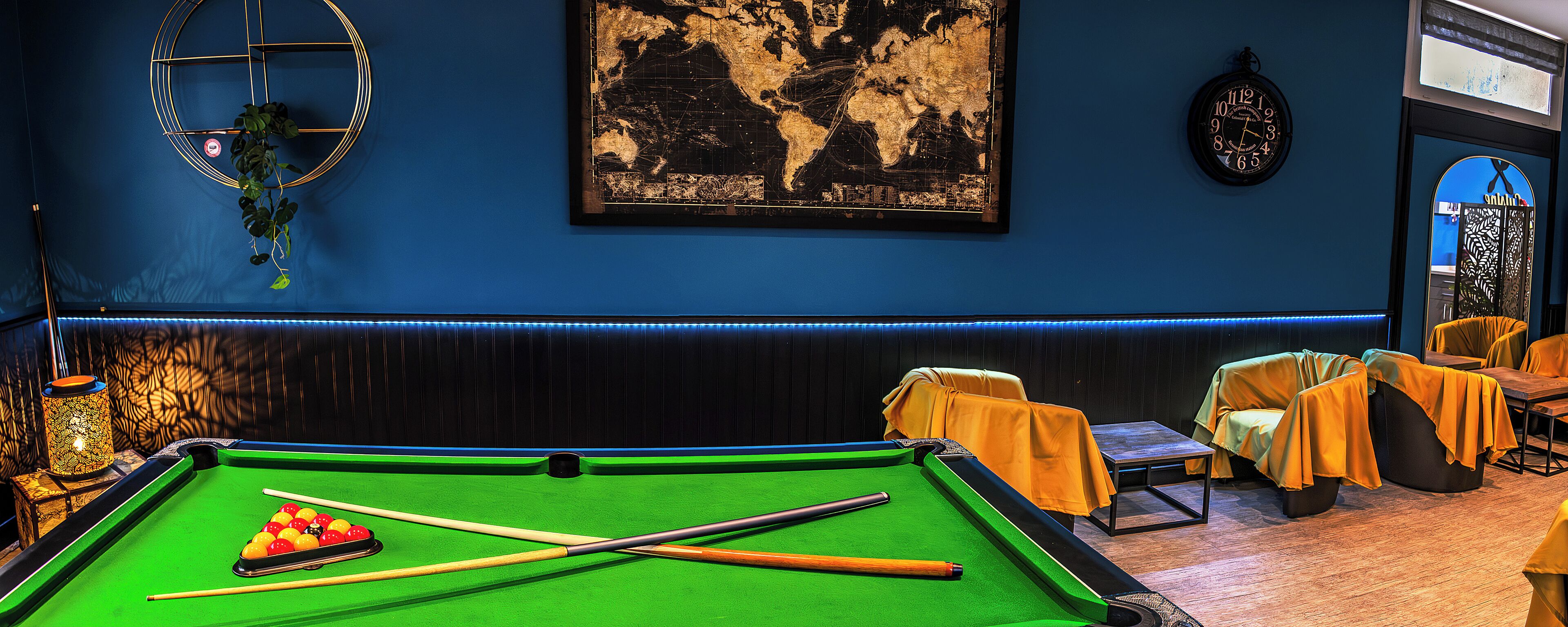 A pool table with balls, a clock, and a world map on the wall.