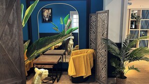 Una habitación con una pared azul decorativa, una estatua de león, una mesa con mantel amarillo y un panel decorativo.
