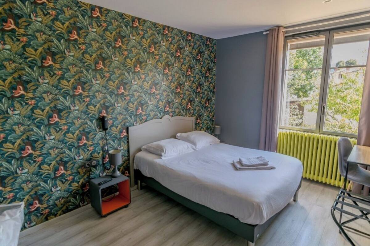 Een slaapkamer met een bed, een stoel, een radiator en een raam met gordijnen.