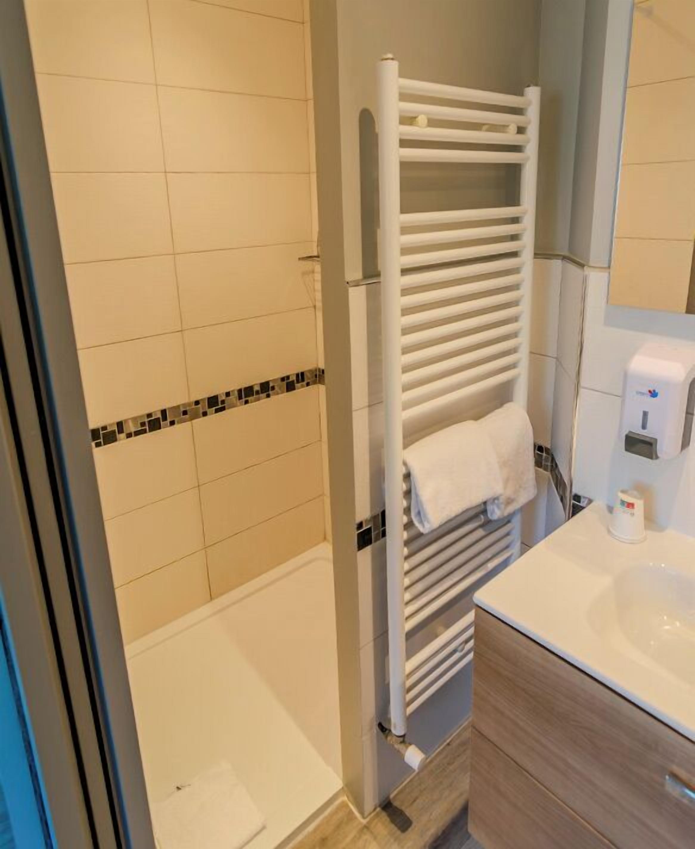 A bathroom with a shower, a white towel rack, a sink, and a mirror.