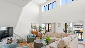 Een ruime woonkamer met een grote flatscreen-tv, een bank, een salontafel, en een eethoek met een houten kast.