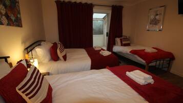 Habitación de hotel con dos camas, ropa de cama roja y blanca, una ventana con cortinas, un cuadro en la pared y una mesita de noche con lámpara.