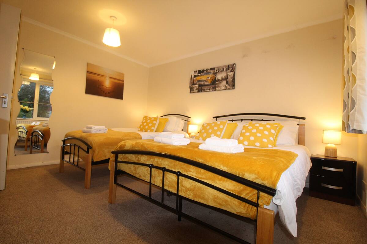 A hotel room with two beds, each with a yellow polka dot pillow and white linens. There is a small bedside table with a lamp, a mirror, and a framed picture on the wall.
