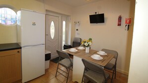 A compact kitchen with a refrigerator, a dining table set for four, and a television mounted on the wall. - Keswick House Chesterfield (Chesterfield)