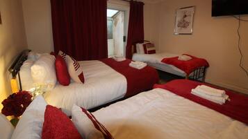 Una habitación de hotel con tres camas, ropa de cama roja y blanca, un televisor en la pared y una ventana con cortinas.