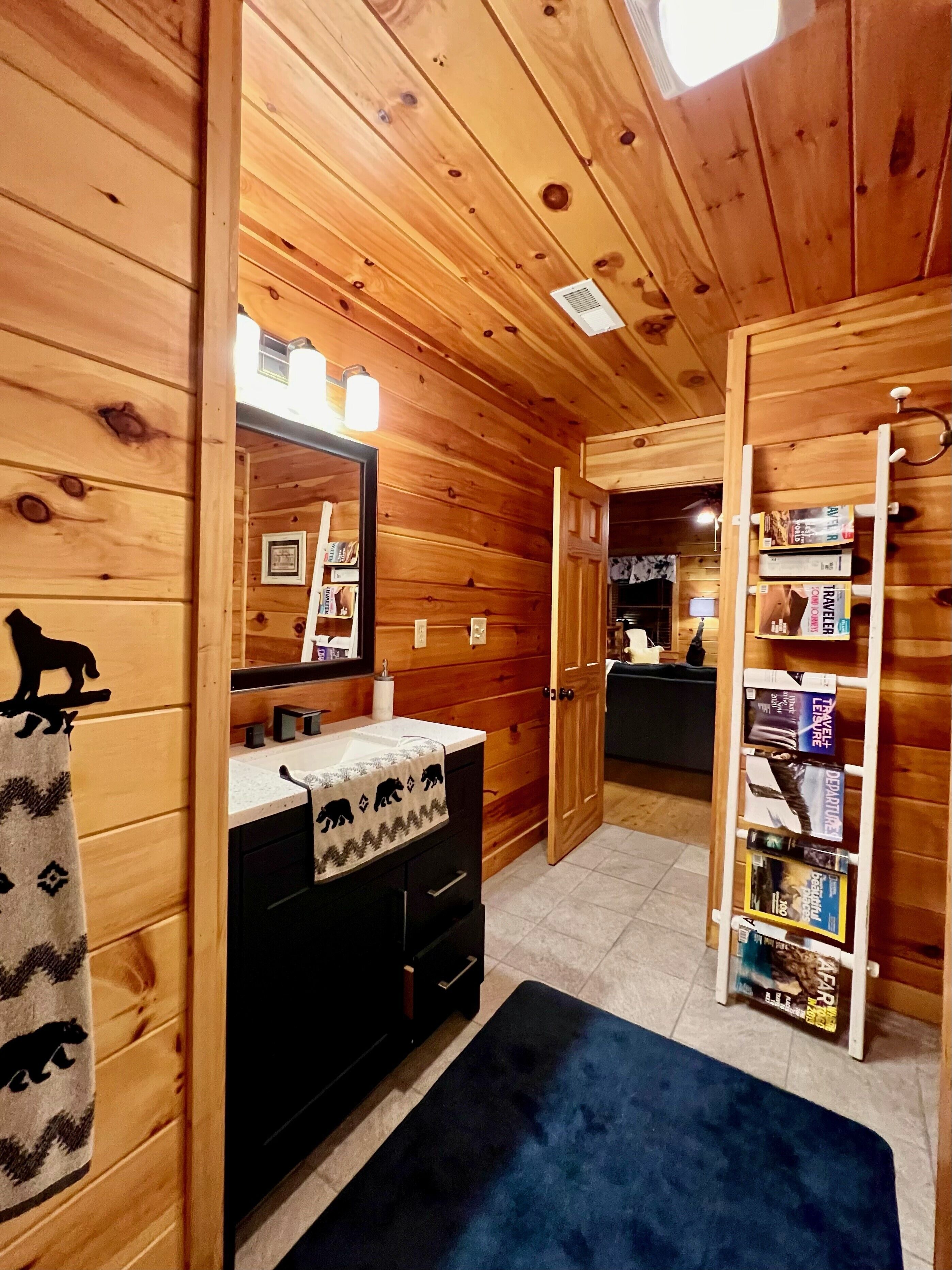 A wooden cabin bathroom with a sink, mirror, and a shelf with books.