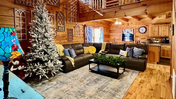 L’intérieur d’un chalet confortable, avec un grand sapin de Noël en bois, un canapé en cuir et un coin repas.