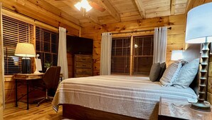 Une chambre dans une cabane en bois, comprenant un lit, un bureau, une chaise, un téléviseur et un ventilateur de plafond.
