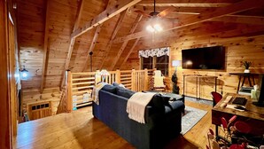 L’intérieur d’un chalet en bois chaleureux et accueillant, avec un canapé, une table à manger, un téléviseur et un escalier.